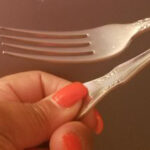 Closeup of a woman's hand holding a steel fork she bent in half during a spoonbending workshop