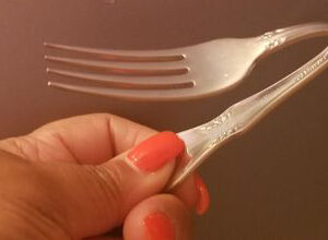 Closeup of a woman's hand holding a steel fork she bent in half during a spoonbending workshop