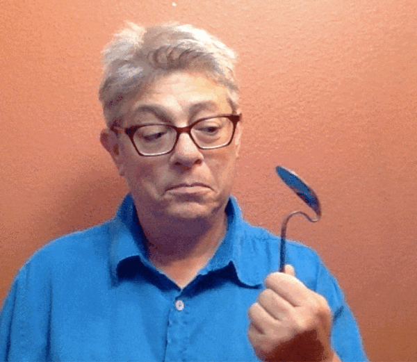 Miche in a blue shirt holding up a bent spoon.