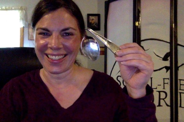 Woman holding her bent spoon next to her cheek after attending SpoonBending Workshop