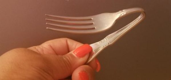 Closeup of a woman's hand holding a steel fork she bent in half during a spoonbending workshop